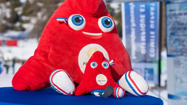 Deux peluches de la mascotte rouge Paris 2024 posées sur une table en extérieur dans une station de ski.
