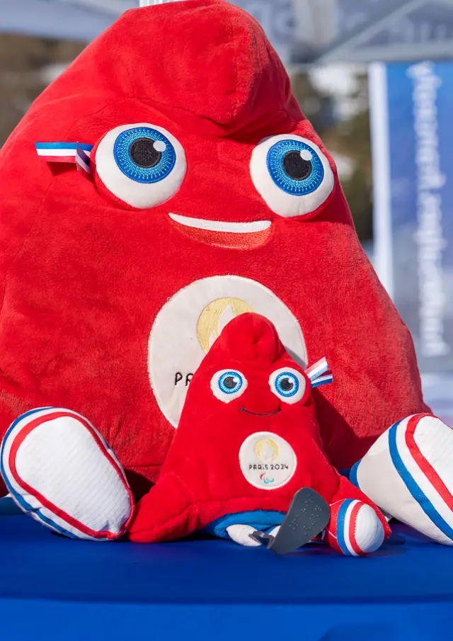Deux peluches de la mascotte rouge Paris 2024 posées sur une table en extérieur dans une station de ski.