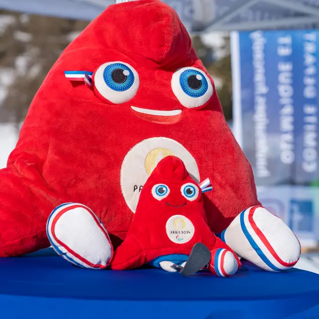 Deux peluches de la mascotte rouge Paris 2024 posées sur une table en extérieur dans une station de ski.