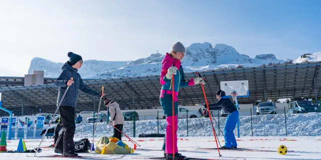 Plusieurs personnes s’initient au ski nordique sur la neige dans un espace sécurisé en station, avec les montagnes en arrière-plan.