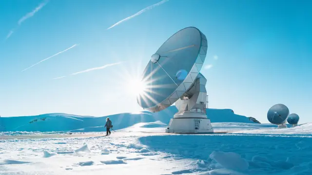 Large scientific satellite dishes on a snowy plateau with low winter sun and blue sky.