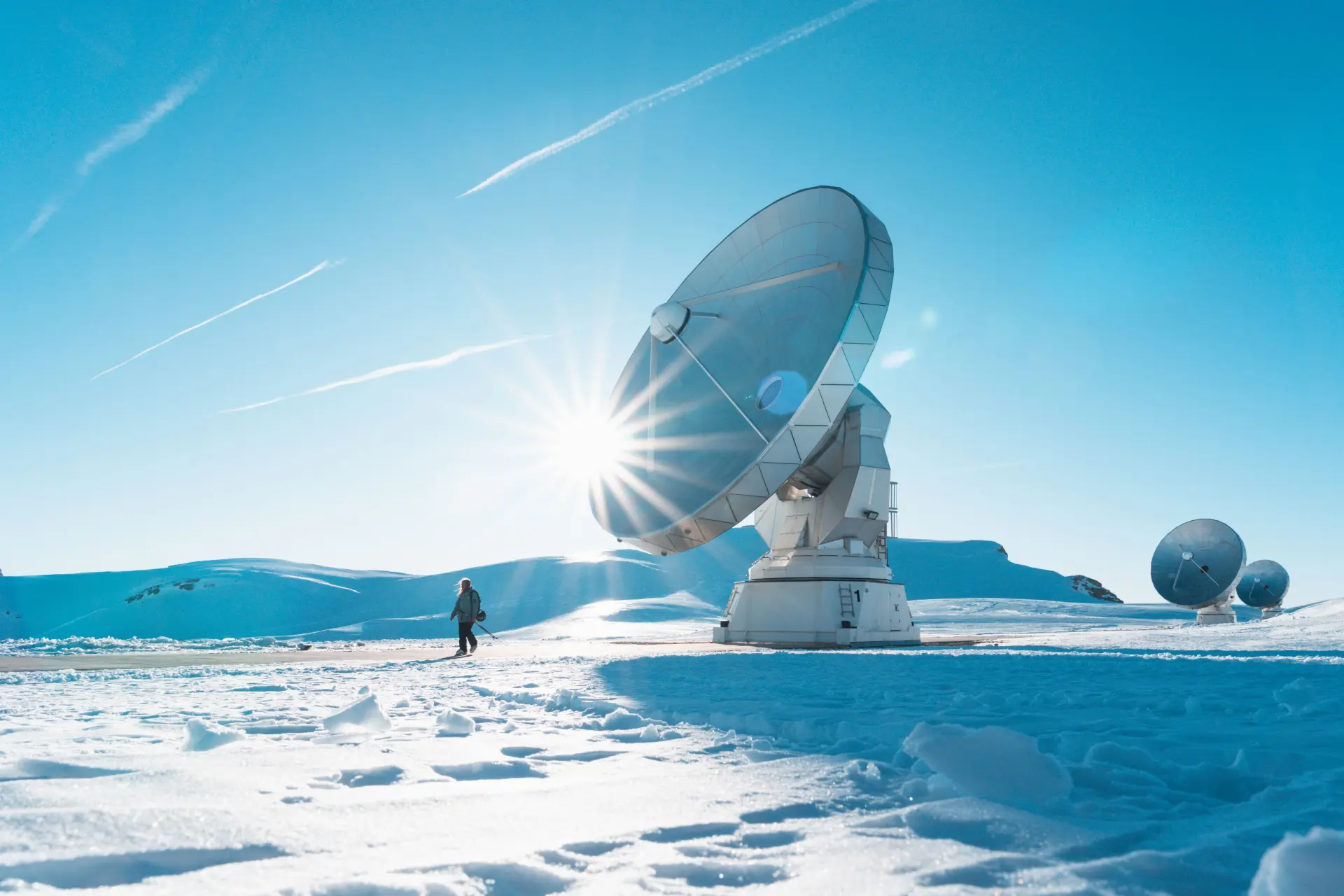 Grandes antennes paraboliques scientifiques sur un plateau enneigé avec soleil rasant et ciel bleu.