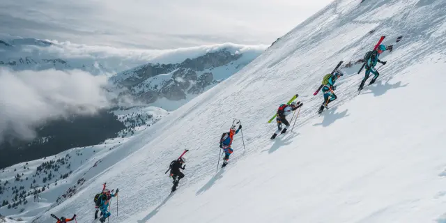 Ski mountaineers ascending a very steep snowy slope with skis strapped to their backpacks during La Grande Trace Winter.
