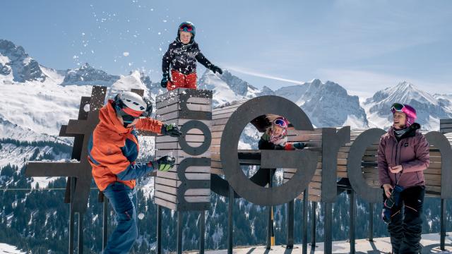 Famille jouant à une bataille de boules de neiges sur le domaine skiable face à la chaîne des Aravis.
