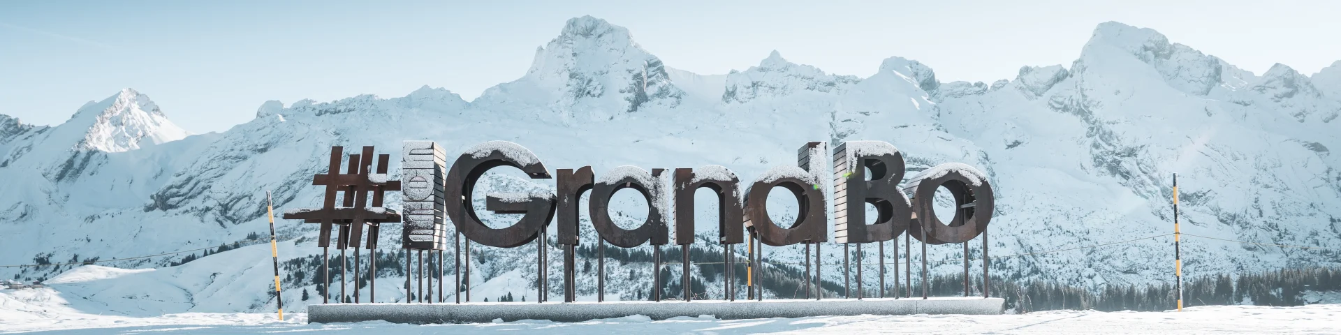 des lettres en bois avec du givre forment le mot mongrandbo devant la chaine des aravis enneigée