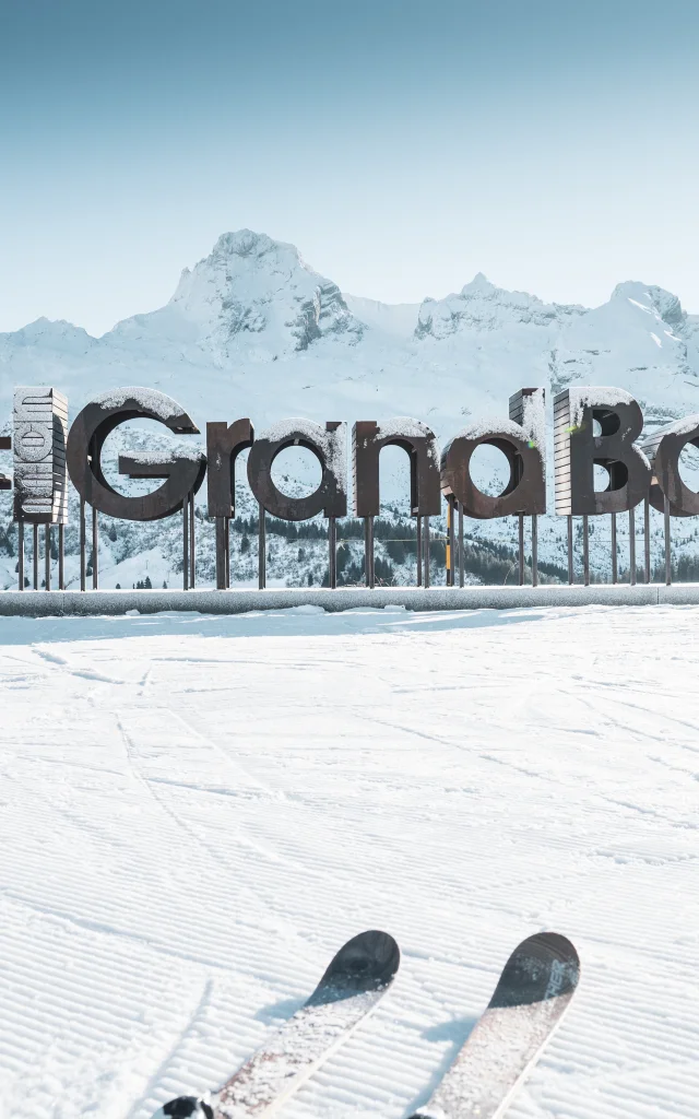 wooden letters with frost form the word mongrandbo in front of the snow-covered aravis range
