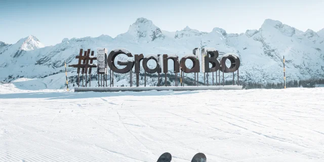 des lettres en bois avec du givre forment le mot mongrandbo devant la chaine des aravis enneigée