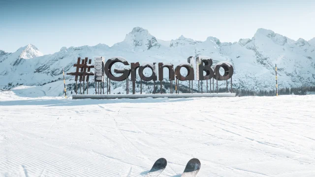 des lettres en bois avec du givre forment le mot mongrandbo devant la chaine des aravis enneigée