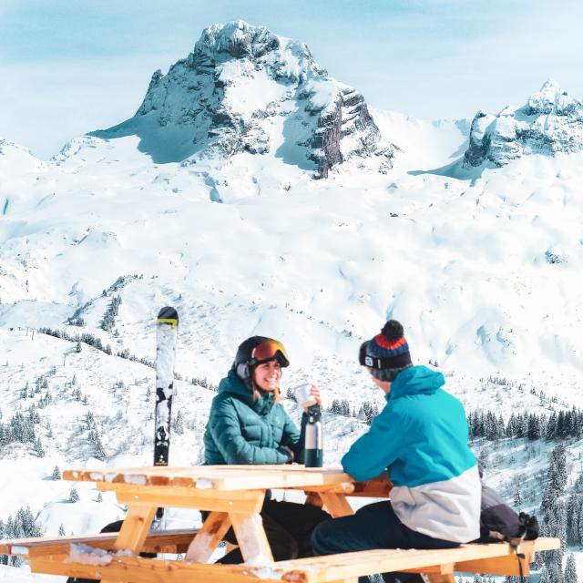 Couple de skieurs buvant une boisson chaude devant la Pointe Percée enneigée