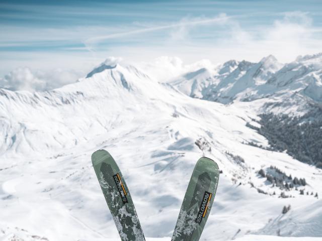 Skis crossed in front of a panoramic view of snow-capped peaks.