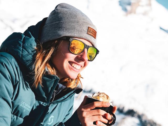 Skieuse tenant un café viennois dans ses mains avec la Pointe Percée pour toile de fond