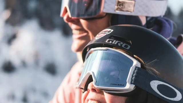 Une mère et son fils sont sur un télésiège pour monter en haut de la piste de ski. Ils sont tous deux très complices et semblent être impatients de skier, au vu de leur grand sourire et expression du visage, contemplant les pistes de ski.