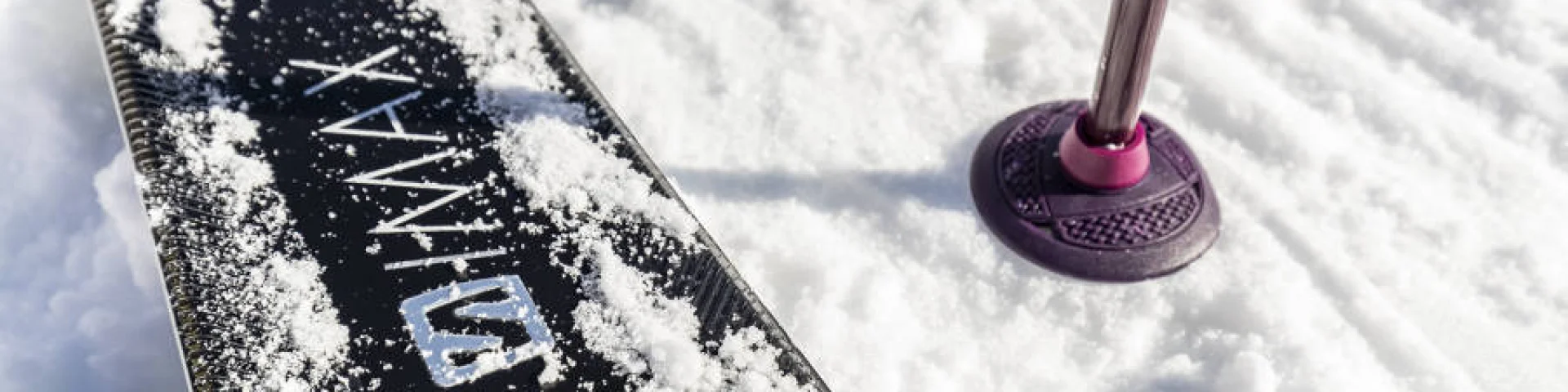 Gros plan sur un ski et un bâton planté dans la neige fraîche au Grand-Bornand, symbole de sports d’hiver et glisse en montagne.
