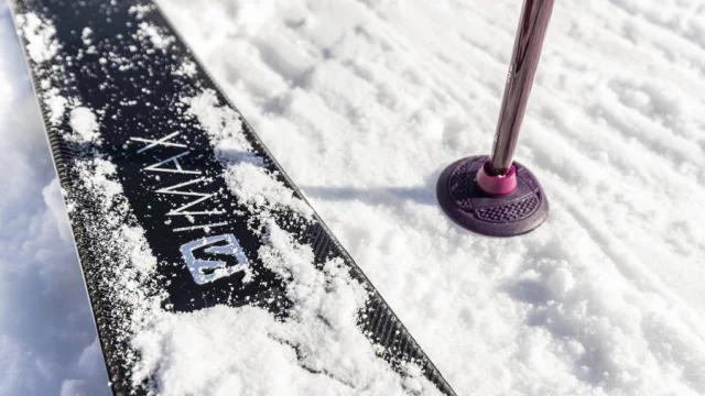 Gros plan sur un ski et un bâton planté dans la neige fraîche au Grand-Bornand, symbole de sports d’hiver et glisse en montagne.