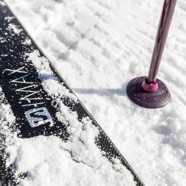 Gros plan sur un ski et un bâton planté dans la neige fraîche au Grand-Bornand, symbole de sports d’hiver et glisse en montagne.