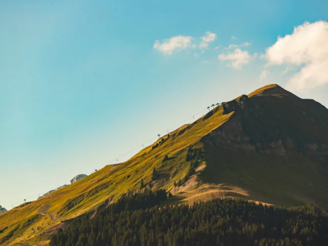 A panoramic view of Mont Lachat in summer, with its lush green meadows and chairlifts leading to the summit.
