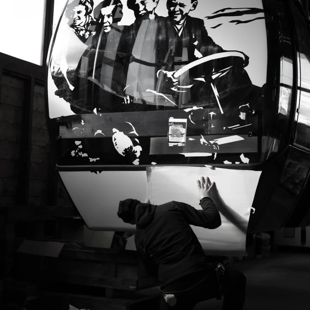 Un artiste en train d'appliquer un décor en noir et blanc sur une cabine de télécabine du Grand-Bornand, projet Grandborama.