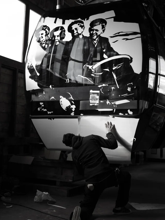 Un artiste en train d'appliquer un décor en noir et blanc sur une cabine de télécabine du Grand-Bornand, projet Grandborama.