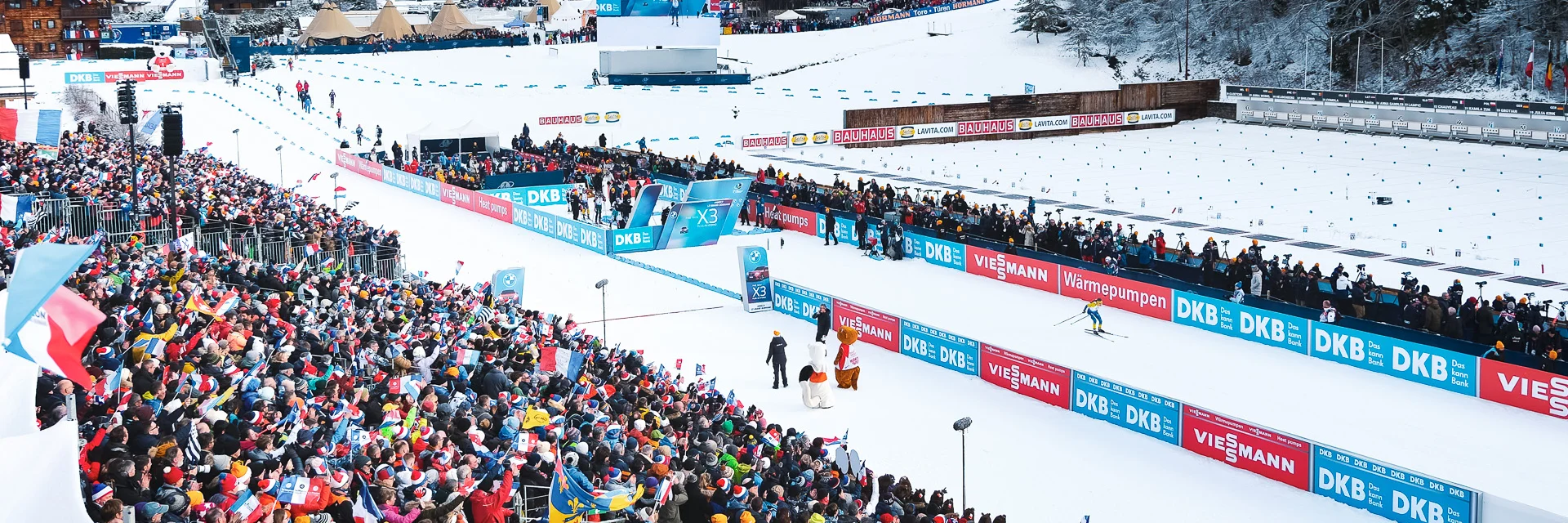 Vue aérienne du stade Sylvie Becaert dans un décor enneigé lors de la Coupe du monde de Biathlon Annecy-Le Grand-Bornand 2024. Nous pouvons voir la ferveur du public dans les gradins.