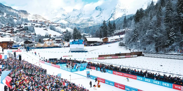 Vue aérienne du stade Sylvie Becaert dans un décor enneigé lors de la Coupe du monde de Biathlon Annecy-Le Grand-Bornand 2024. Nous pouvons voir la ferveur du public dans les gradins.