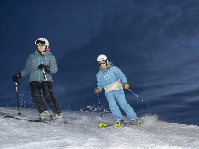 Deux skieurs profitant de la piste alpine du Charmieux, descente en ski nocturne sous un ciel étoilé au Grand-Bornand.