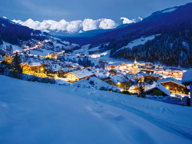Panorama nocturne du Grand-Bornand, avec les lumières du village scintillant sous les sommets enneigés.