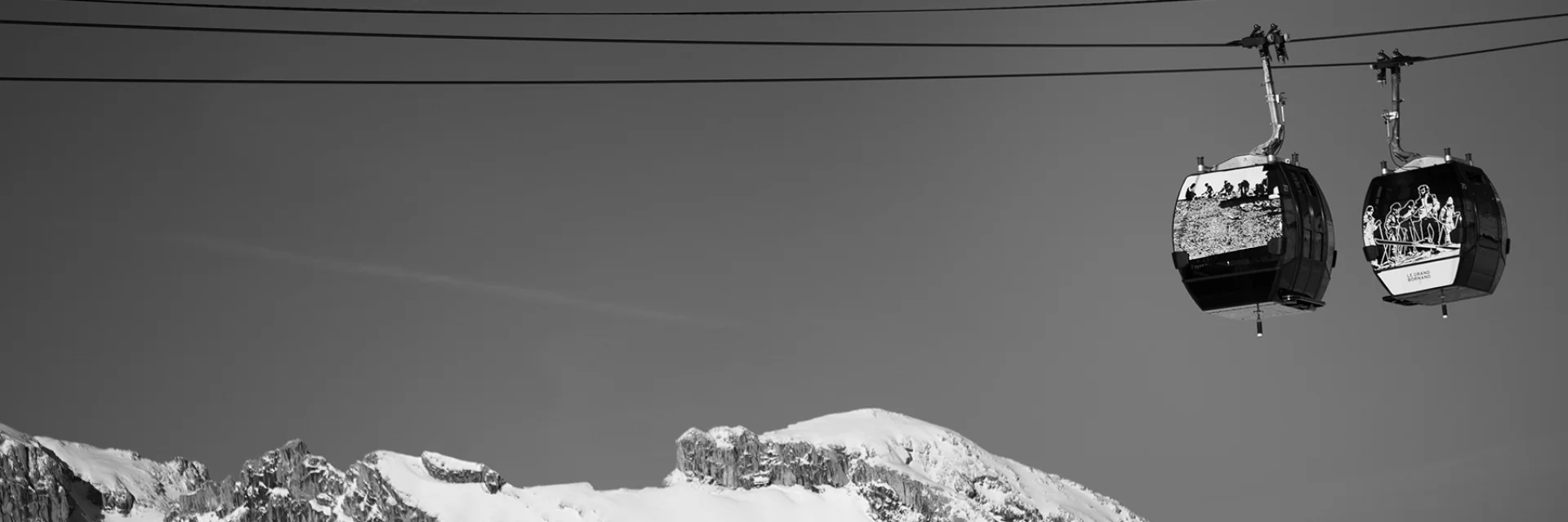 Deux cabines du Grandborama suspendues, décorées d’œuvres artistiques, avec en arrière-plan les sommets enneigés du Grand-Bornand.