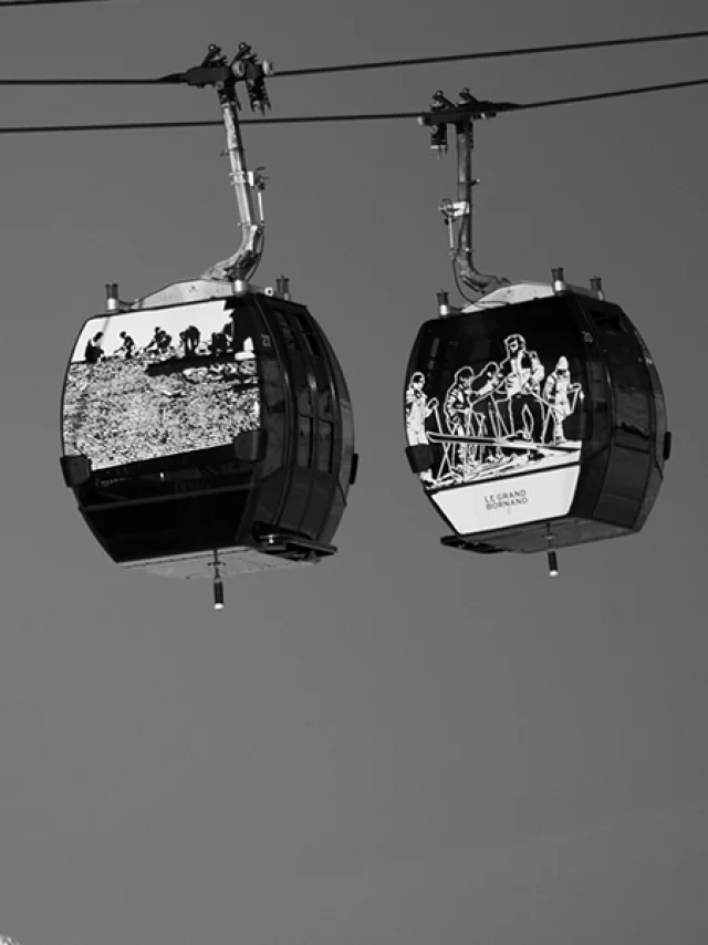 Deux cabines du Grandborama suspendues, décorées d’œuvres artistiques, avec en arrière-plan les sommets enneigés du Grand-Bornand.