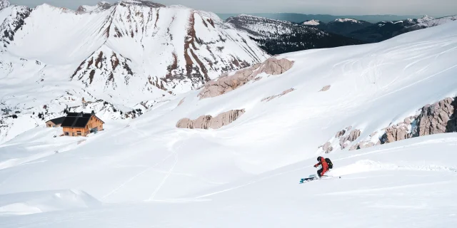 A skier makes a turn in a vast expanse of virgin snow above the pointe percée refuge and the col des annes.
