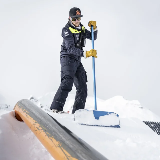 un shaper sculpte l'entrée sur un tube de slide avec sa pelle pour le snowpark du grand-bornand