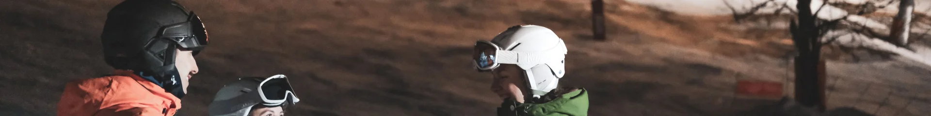 Un groupe de skieurs trinque en terrasse, derrière eux se trouve une piste de ski nocturne éclairée ainsi qu'un télésiège