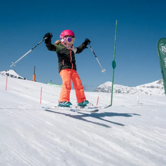 Skifahrendes Kind, das bei blauem Himmel einen Sprung auf dem Môm'Park in Le Grand-Bornand macht.