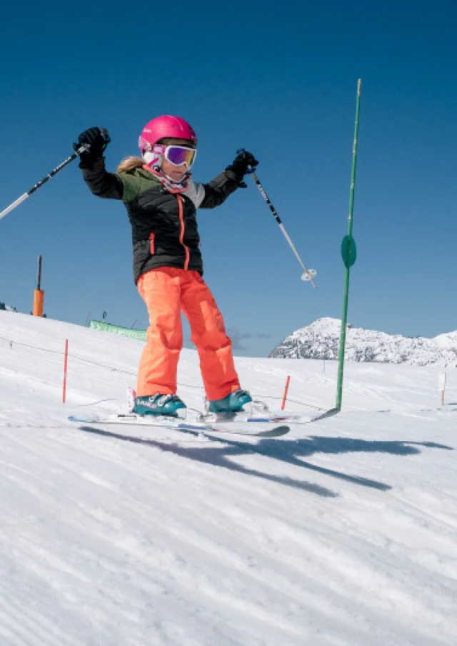 Enfant skieuse effectuant un saut sur le Môm’Park au Grand-Bornand sous un ciel bleu.