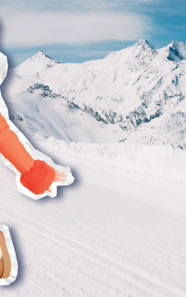 A smiling woman in an orange jacket and white trousers jumps up and down holding a Magic Pass, with a panorama of snow-capped mountains in the background.