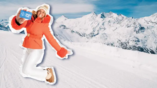 Eine lächelnde Frau in einer orangefarbenen Jacke und einer weißen Hose springt vor Freude auf und ab, während sie einen Magic Pass in der Hand hält, während im Hintergrund ein Panorama mit schneebedeckten Bergen zu sehen ist.