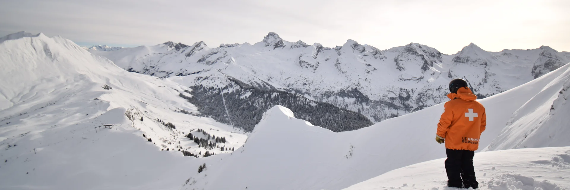 a ski patrolman in front of the aravis range and the immaculate white maroly ridges, at the top of the freeride piste