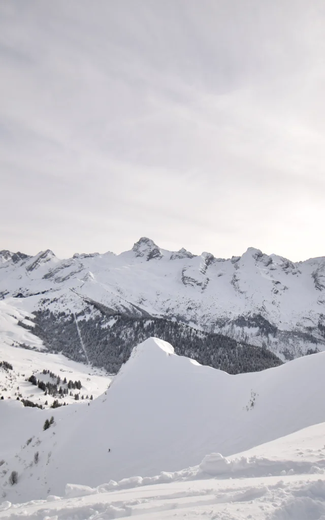 a ski patrolman in front of the aravis range and the immaculate white maroly ridges, at the top of the freeride piste