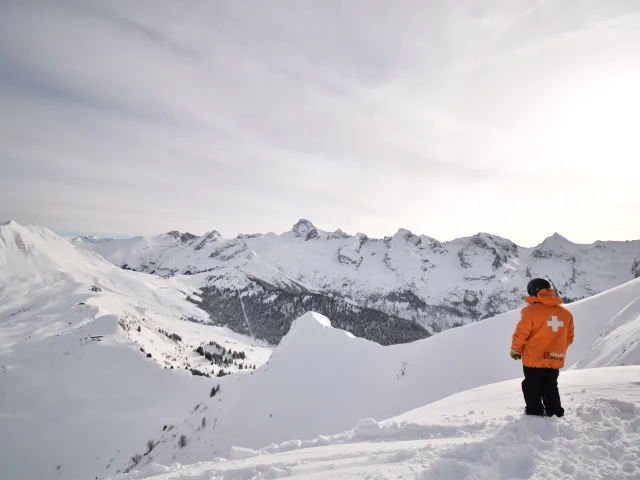 a ski patrolman in front of the aravis range and the immaculate white maroly ridges, at the top of the freeride piste