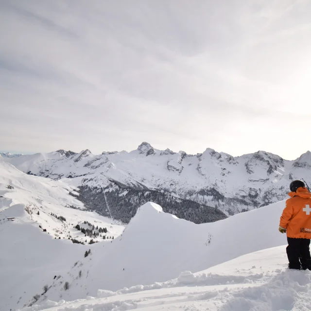 un pisteur secouriste devant la chaine des aravis et les crêtes du maroly d'un blanc immaculé, il se trouve au sommet de la piste la freeride