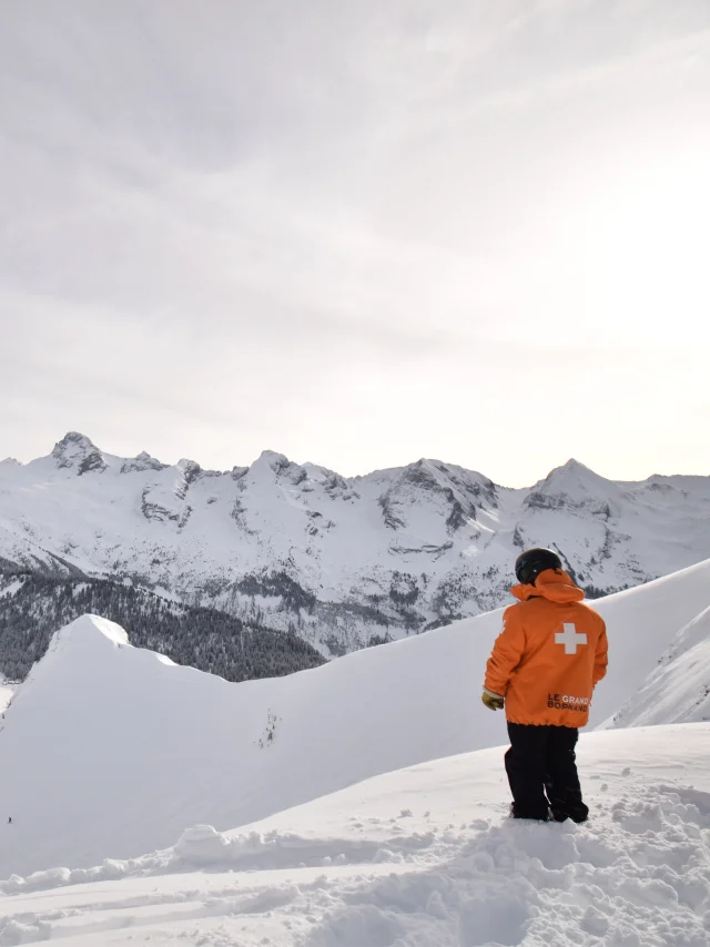 un pisteur secouriste devant la chaine des aravis et les crêtes du maroly d'un blanc immaculé, il se trouve au sommet de la piste la freeride