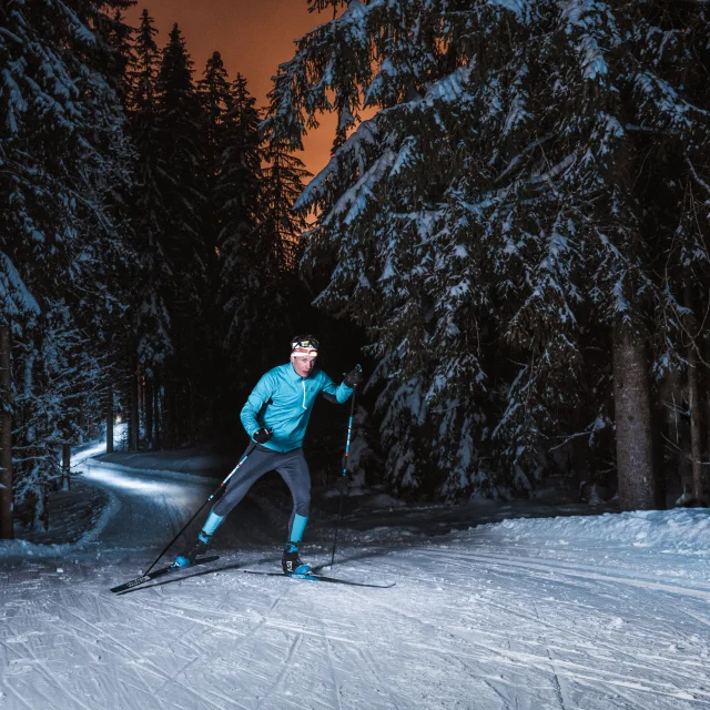 a skier on a nordic ski slope in grand-bornand at night in a snow-covered forest under an orange sky