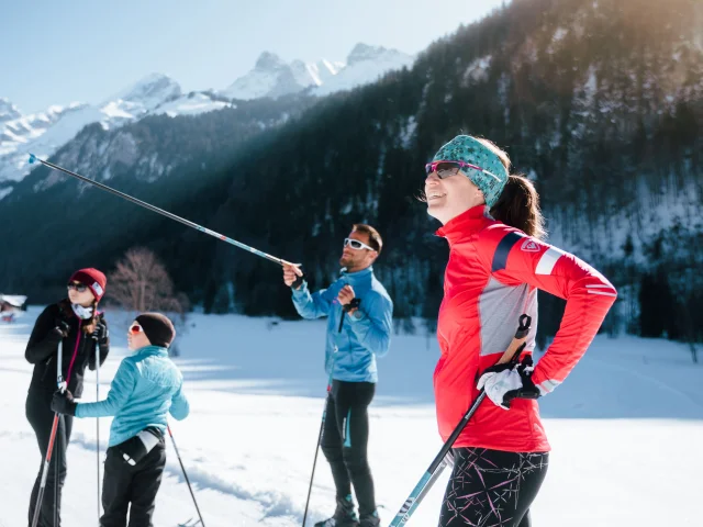 Eine Familie von Langläufern genießt eine Pause in der Sonne, umgeben von schneebedeckten Bergen. Die Stimmung ist entspannt und fröhlich.