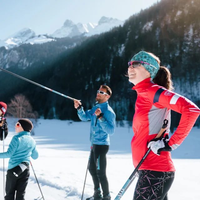 Une famille de skieurs de fond profite d'une pause sous le soleil, entouré de montagnes enneigées. L'ambiance est détendue et joyeuse.