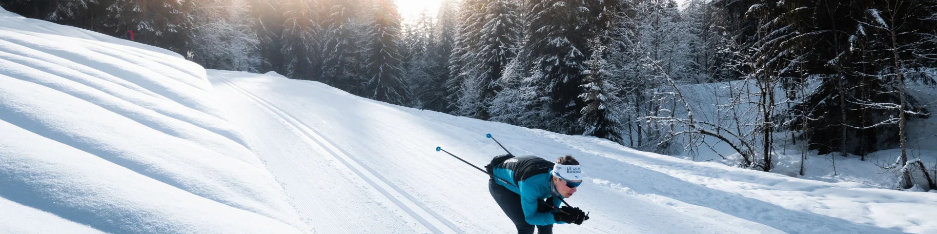 Un skieur de fond sur une piste de ski nordique du Grand-Bornand en position de schuss dans les traces de classiques au milieu d'une forêt einneigée