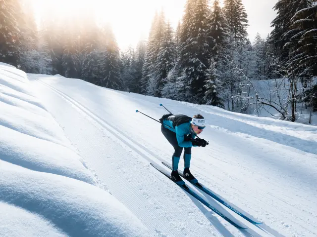 A cross-country skier on a Nordic ski run in Le Grand-Bornand in a schuss position in the classic tracks in the middle of a snow-covered forest.
