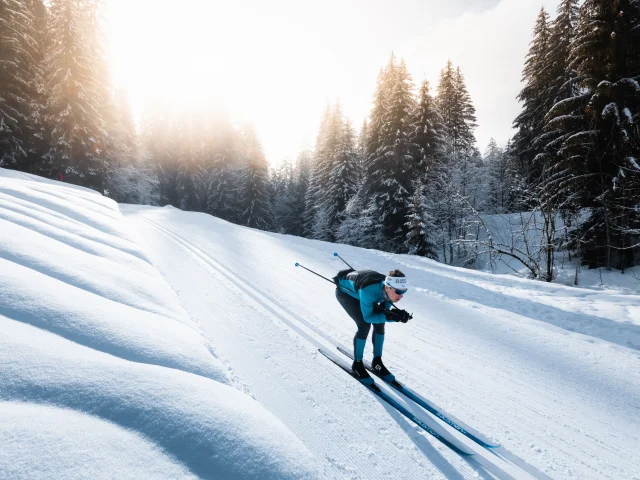A cross-country skier on a Nordic ski run in Le Grand-Bornand in a schuss position in the classic tracks in the middle of a snow-covered forest.