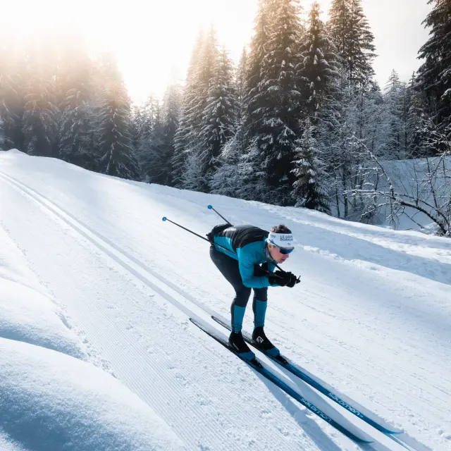 Un skieur de fond sur une piste de ski nordique du Grand-Bornand en position de schuss dans les traces de classiques au milieu d'une forêt einneigée