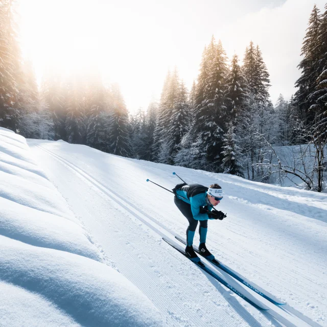 A cross-country skier on a Nordic ski run in Le Grand-Bornand in a schuss position in the classic tracks in the middle of a snow-covered forest.
