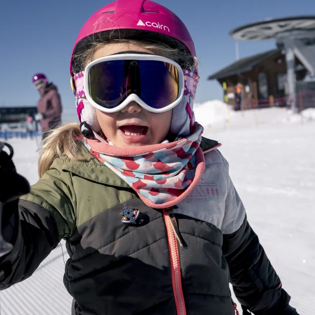 Photo d'une enfant au ski en gros plan avec en arrière plan des installations de remontées mécaniques.