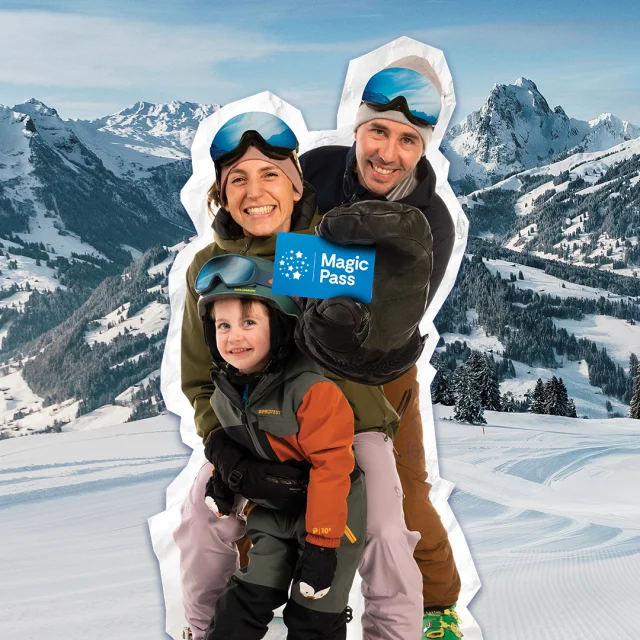Deux parents et leur enfant avec le sourire équipés pour le ski tiennent dans leur main un magic pass devant un paysage de montagnes enneigées